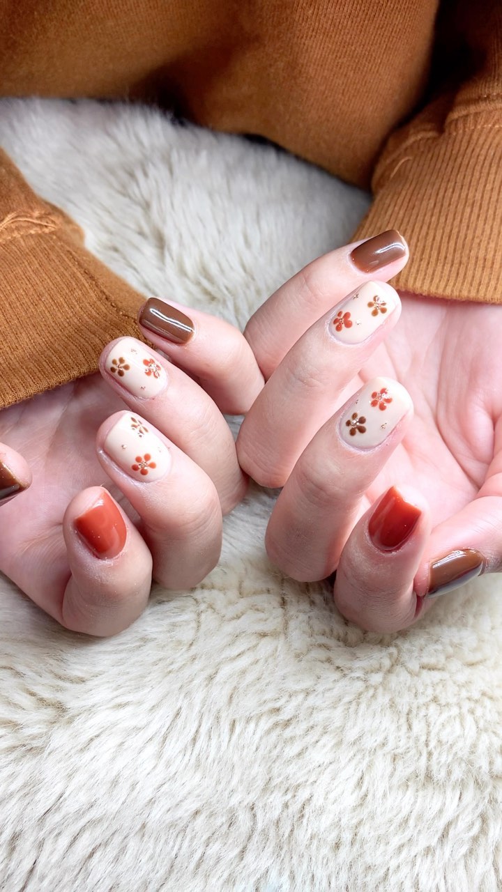 Uñas en tonos marrón, óxido y crema con florcitas pintadas a mano